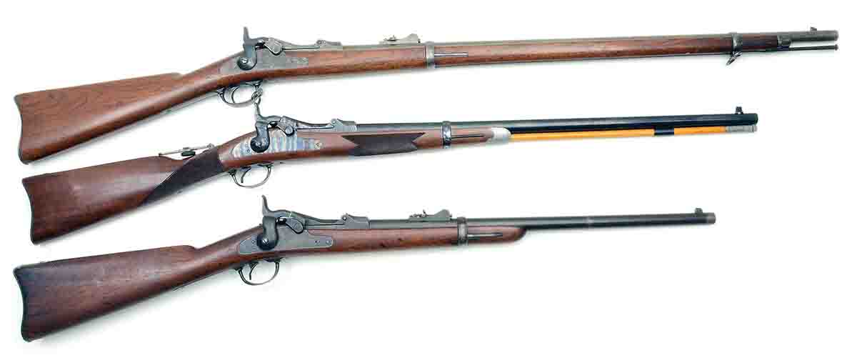 These are the basic configurations of U.S. Model 1873 trapdoor .45s. Top is a standard infantry rifle. Bottom is a standard cavalry carbine. Between them is a replica of the Officer’s Model made by the H&R Company in the 1970s.
